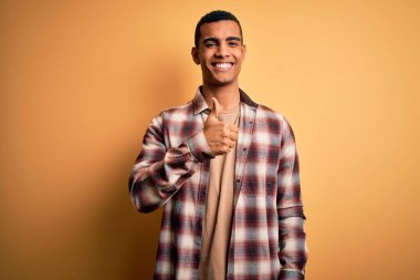 Sarı arka planda sıradan bir gömlek giyen genç, Afro-Amerikan bir adam elleriyle mutlu bir jest yapıyor. Kameraya bakıp başarıyı gösteren ifade onaylanıyor.