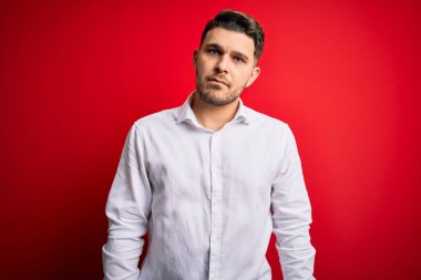 Kırmızı izole edilmiş arka plan üzerinde duran mavi gözlü genç iş adamı yüzünde ciddi bir ifadeyle rahatladı. Basit ve doğal bir şekilde kameraya bakıyorsun..