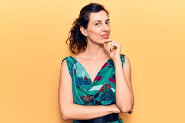 Gündelik giysiler giyen genç, İspanyol bir kadın kameraya kollarını kavuşturup, çenesine dokunarak gülümsüyor. Olumlu düşünmek. 