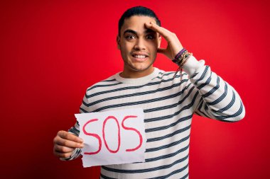 Kırmızı arkaplandaki afişi tutmakta zorlanan genç Brezilyalı adam el ele, utanç ve şaşkınlık dolu, sinirli ve hayal kırıklığına uğramış bir şekilde vurguladı. Hata için korku ve üzüntü.