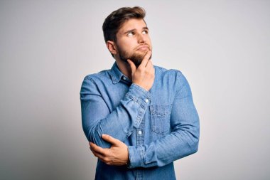 Sakallı, mavi gözlü, eli çenesinde sıradan bir kot gömlek giyen, soru soran, düşünceli bir sarışın genç. Düşünceli bir yüzle gülümsüyor. Şüphe kavramı.