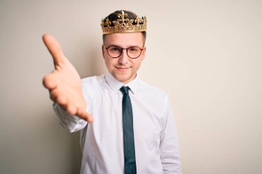 İzole edilmiş arka planda altın taç takan yakışıklı beyaz iş adamı dostça bir selamlama ve hoş geldin hediyesi olarak gülümsüyor. Başarılı bir iş..