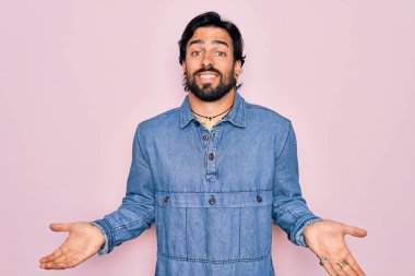 Pembe arka planda hippi tarzı giyinen yakışıklı, bohem bir adam. Kolları ve elleri havada, kafası karışmış bir ifade. Şüphe kavramı.