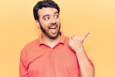 Gündelik giysiler giymiş genç İspanyol bir adam baş parmağını yana kaldırıyor ve ağzı açık gülümsüyor. 