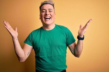 Sarı arka plan üzerine gündelik yeşil tişört giyen genç ve modern bir adam çılgın ve başarıyı kollarını kaldırıp heyecanla haykırarak kutluyor. Kazanan konsept