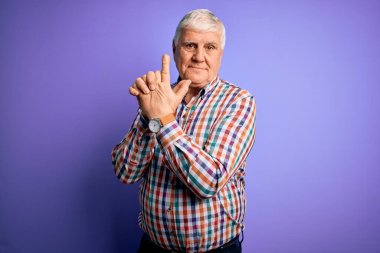 Kıdemli yakışıklı, beyaz gömlekli, yalıtılmış mor arka planda, sembolik silahı olan, el hareketleriyle silah tutan, ateş eden, kızgın yüzlü, yaşlı bir adam.