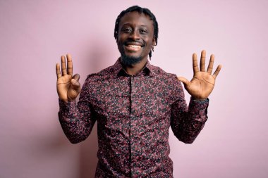 Genç, yakışıklı, Afro-Amerikalı bir adam pembe arka planda dikilmiş gülümseyen, kendinden emin ve mutlu bir şekilde sekiz numarayı işaret ediyor..