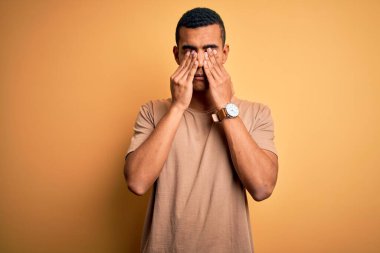 Genç, yakışıklı, Afro-Amerikan bir adam, günlük tişörtler giymiş, sarı arka planda duruyor. Yorgunluk ve baş ağrısı için gözlerini ovuşturuyor, uykulu ve yorgun bir ifade takınıyor. Görüş sorunu