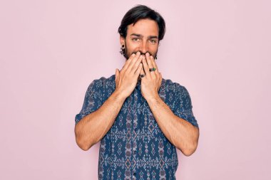 Yakışıklı İspanyol bohem adam pembe arka planda hippi tarzı giyinmiş gülüyor ve utanıyor kıkırdıyor elleri, dedikoduları ve skandalları ağızlarına tıkıyor.