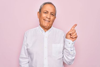 Soyutlanmış pembe arka planda zarif gömlekler giyen yakışıklı bir adam. Yüzünde kocaman bir gülümseme var. Elleri ve parmakları kameraya bakıyor..