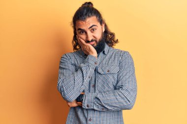 Gündelik kıyafetler giyen genç Arap adam kollarını kavuşturarak depresyondan yorgun ve sıkılmış göründüğünü düşünüyor.. 