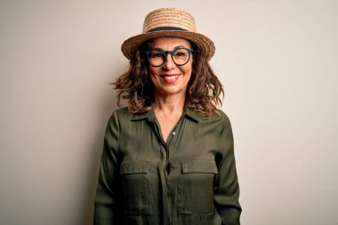 Gözlüklü ve şapkalı orta yaşlı esmer kadın izole edilmiş beyaz arka planda mutlu ve havalı bir gülümsemeyle dikiliyor. Şanslı kişi..