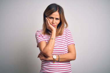 Orta yaşlı güzel bir kadın izole edilmiş beyaz arka plan üzerine sıradan çizgili tişört giyip kollarını kavuşturarak depresyondan sıkılmış ve yorgun göründüğünü düşünüyor..