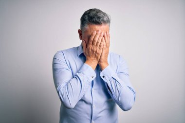 Orta yaşlı, yakışıklı, gri saçlı, beyaz arka planda zarif bir gömlek giyen, ağlarken yüzünü ellerle kapatan bir iş adamı. Depresyon kavramı.