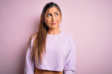 Pembe izole edilmiş arka plan üzerine kazak giyen genç ve güzel bir kadın gülümsüyor ve başka tarafa bakıyor..