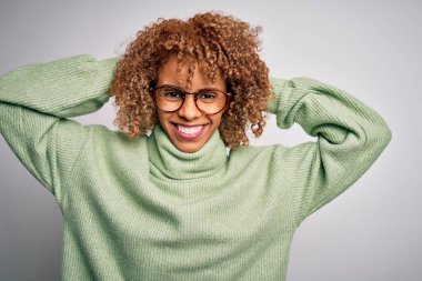 Güzel Afro-Amerikan kadın balıkçı yaka kazak giyiyor ve gözlük takıyor rahatlıyor ve esniyor, kolları ve elleri başının arkasında ve boynunda gülümsüyor.