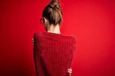 Genç, güzel, kızıl saçlı bir kadın izole edilmiş kırmızı arka plan üzerine gündelik süveter giyip kendine mutlu ve pozitif bir şekilde sarılıyor. Sevgi ve özgüven.