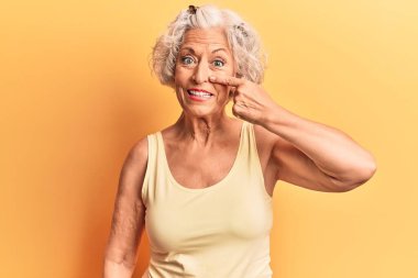 Yaşlı, gri saçlı, günlük kıyafetler giyen, el parmağı ve burnu olan, neşeli gülümseyen bir kadın. güzellik konsepti 