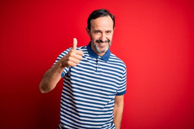 Orta yaşlı, beyaz, sıradan çizgili polo giyen, izole edilmiş kırmızı arka planda duran, el hareketleriyle mutlu mesut hareket eden bir adam. Kameraya bakıp başarıyı gösteren ifade onaylanıyor.