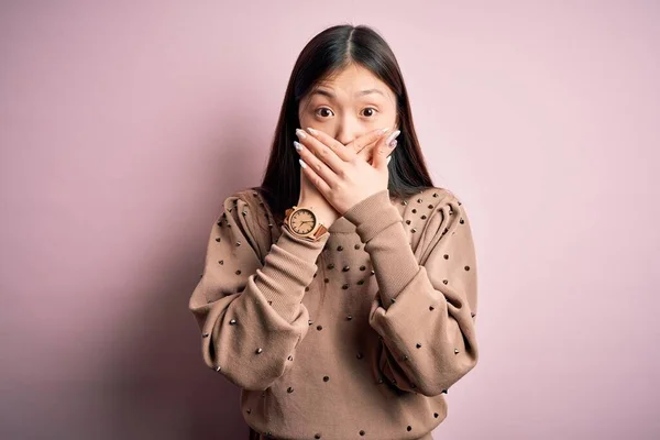 年轻美丽的亚洲女人穿着时尚和雅致的毛衣 穿着粉色的 舒适的背景 双手捂着嘴 为错误而震惊 秘密概念 — 图库照片