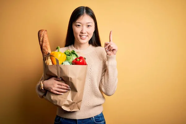 Mladá Asiatka Drží Papírový Sáček Čerstvými Zdravými Potravinami Přes Žluté — Stock fotografie