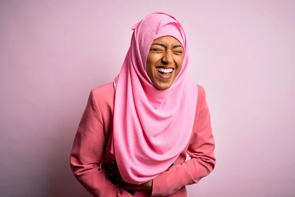 Young African American afro woman wearing muslim hijab over isolated pink background smiling and laughing hard out loud because funny crazy joke with hands on body.
