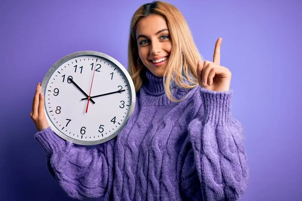 Young Beautiful Blonde Woman Doing Countdown Holding Big Clock Purple — Stock Photo, Image