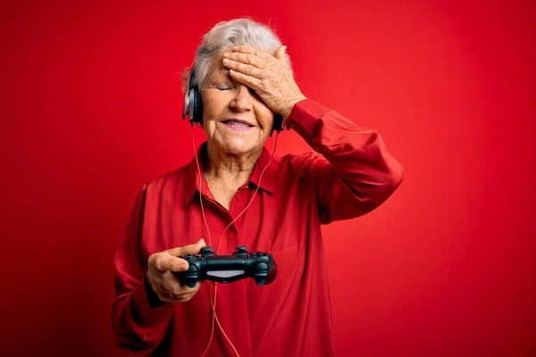 年长的漂亮的白发游戏女玩家用操纵杆和耳机玩电子游戏 手头上的压力很大 满脸羞愧和惊讶 愤怒和沮丧 恐惧和因错误而烦恼 — 图库照片