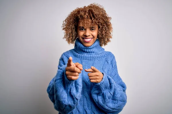 Beyaz arka plan üzerine balıkçı yaka kazak giyen güzel Afro-Amerikan kadın mutlu ve komik yüzlü parmaklarını kameraya doğrultuyor. İyi enerji ve titreşimler.