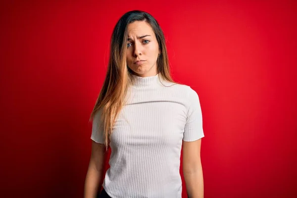 Beautiful blonde woman with blue eyes wearing casual white t-shirt over red background depressed and worry for distress, crying angry and afraid. Sad expression.