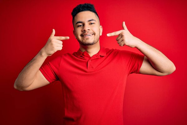 Young handsome man wearing red casual polo standing over isolated background smiling cheerful showing and pointing with fingers teeth and mouth. Dental health concept.