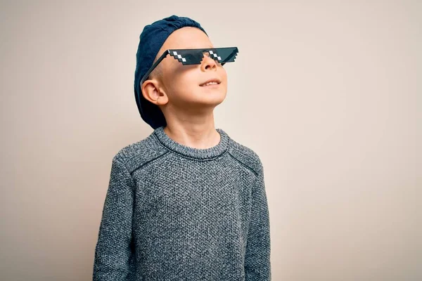 Young little caucasian kid wearing internet meme thug life glasses over isolated background looking away to side with smile on face, natural expression. Laughing confident.