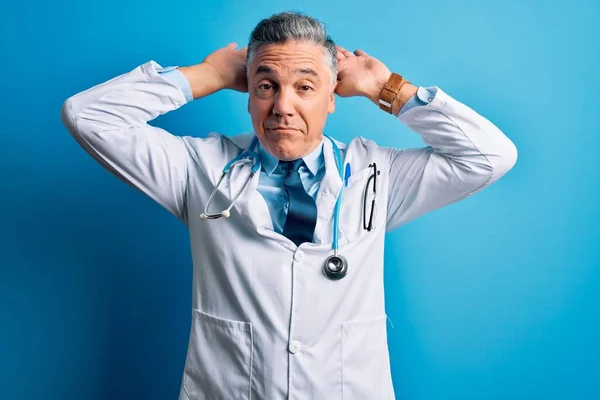 Middle age handsome grey-haired doctor man wearing coat and blue stethoscope Doing bunny ears gesture with hands palms looking cynical and skeptical. Easter rabbit concept.