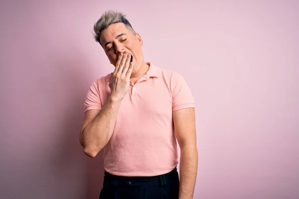 孤立した背景にカジュアルなピンクのTシャツを着た若いハンサムな現代人は 手で口をカバー疲れYawning退屈 眠れないのか — ストック写真