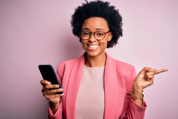 Young African American afro woman with curly hair having conversation using smartphone very happy pointing with hand and finger to the side