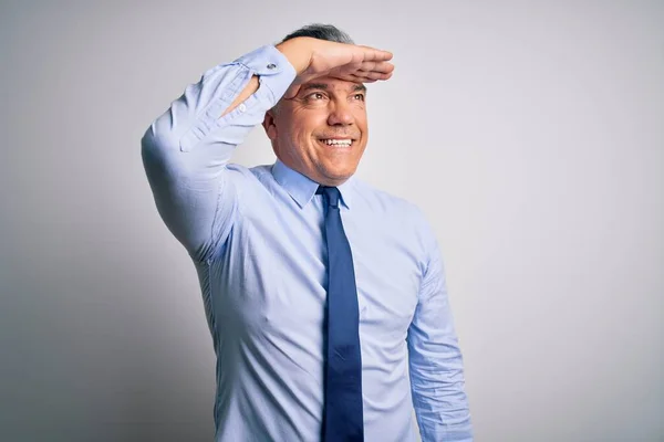 Middle age handsome grey-haired business man wearing elegant shirt and tie very happy and smiling looking far away with hand over head. Searching concept.