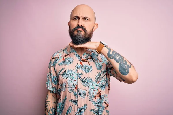 Sakallı ve dövmeli yakışıklı, pembe arka planda sıradan bir çiçek gömleği giyen, boğazını bıçak niyetine kesen, saldırganlığı şiddetle tehdit eden bir adam.