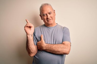 Orta yaşlı, beyaz tişörtlü yakışıklı adam izole edilmiş beyaz arka planda duruyor. Yüzünde kocaman bir gülümseme var. Eli ve parmağı kameraya bakıyor..