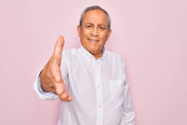 Soyutlanmış pembe arka planda zarif tişörtler giyen yaşlı, yakışıklı, gri saçlı adam dostça bir selamlama ve hoş geldin hediyesi olarak gülümsüyor. Başarılı bir iş..