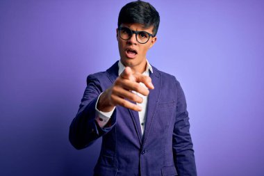 Ceket ve gözlük takan genç yakışıklı iş adamı mor arka planda rahatsız ve hayal kırıklığına uğramış, sana kızgın ve kızgın.