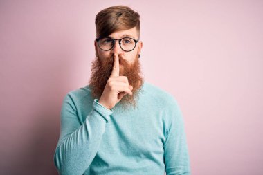 Pembe soyutlanmış arka planda gözlüklü, sakallı yakışıklı kızıl saçlı yakışıklı adam sessiz olmak istiyor. Sessizlik ve gizli konsept.