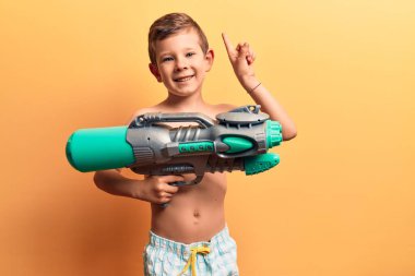 Mayo giyen tatlı sarışın çocuk elinde su tabancası ile gülümsüyor ya da bir soru işareti yapıyor mutlu bir yüzle, bir numara 