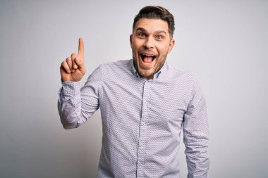 Tecrit edilmiş arka planda duran mavi gözlü genç iş adamı başarılı bir fikir işaret ediyor. Heyecanlı ve mutlu. Bir numara..