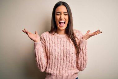 Genç, güzel esmer kadın, izole edilmiş beyaz arka plan üzerine gündelik kazak giyip kollarını kaldırmış ve gözleri kapalı heyecanla haykırarak başarı için deli ve çılgın bir kutlama yapıyor. Kazanan konsept