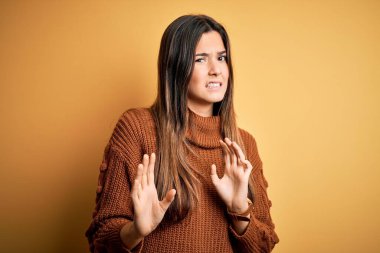 İzole edilmiş sarı arka planda duran sıradan süveter giyen genç ve güzel bir kız tiksinti reaksiyonu yüzünden tiksindirici ve rahatsız edici bir ifade takınıyor. Eller havada