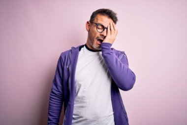 Pembe arka planda duran mor eşofman üstü ve gözlüklü genç yakışıklı adam esnemekten yorgun düşmüş yüzünü, gözünü ve ağzını eliyle kapatıyor. Yüzüm acıyor..