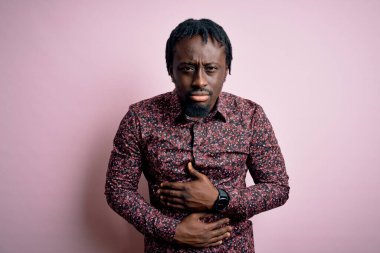 Genç, yakışıklı, Afro-Amerikalı bir adam pembe arka planda dikilmiş, midesi ağrıyan, hazımsızlık çeken, ağrılı bir hastalık yüzünden rahat duramıyor. Ache kavramı.
