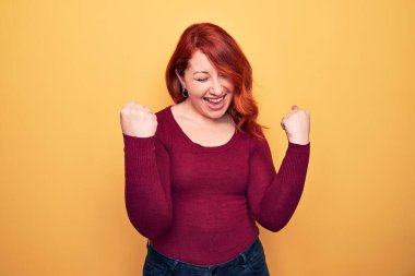 Sarı arka planda sıradan bir süveter giyen genç ve güzel bir kadın kolları havada ve gözleri kapalı bir şekilde başarıyı kutluyor ve şaşırıyor.