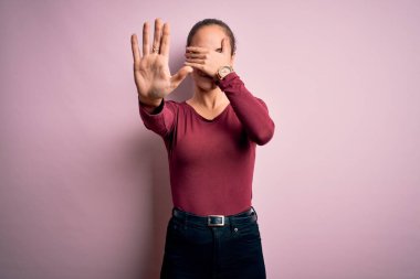 Gündelik tişört giyen genç ve güzel bir kadın izole edilmiş pembe arka plan üzerinde duruyor gözleri ellerle örtüyor ve üzgün ve korku ifadeleriyle dur hareketi yapıyor. Utanç verici ve olumsuz bir kavram..