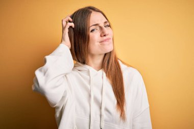 Genç, güzel, kızıl saçlı sporcu kadın izole edilmiş sarı arka plan kafa karıştırıcı ve soru sormayı merak eden bir kazak giyiyor. Şüpheyle kararsız, kafa kafaya düşünerek. Düşünceli kavram.